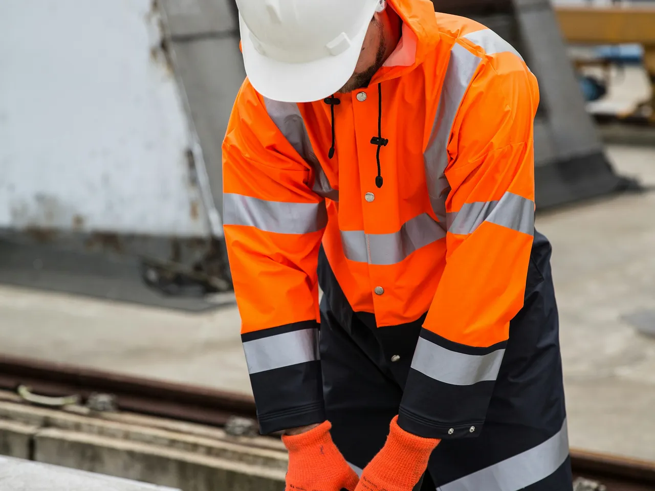 Opérateur en veste haute visibilité orange travaillant sur une structure métallique